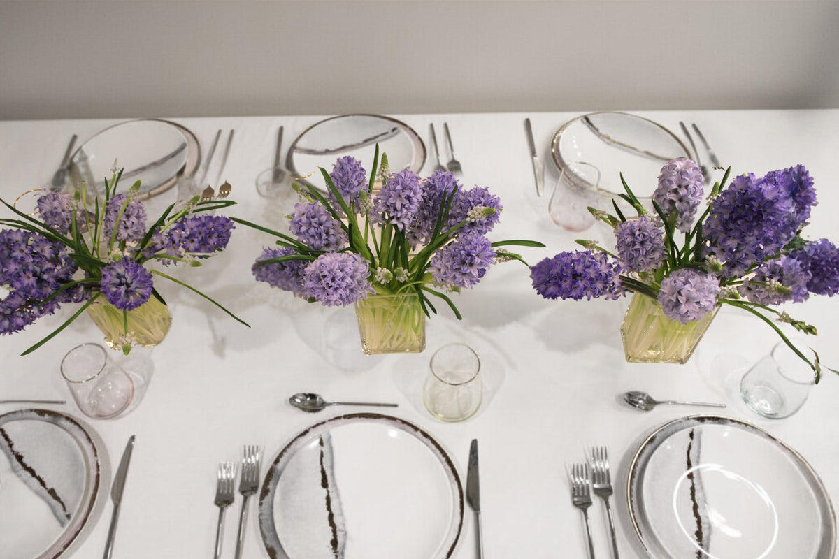 Table scape of 3 arrangements containing purple/blue hyacinths and white muscari in clear glass 3x4x6" vase