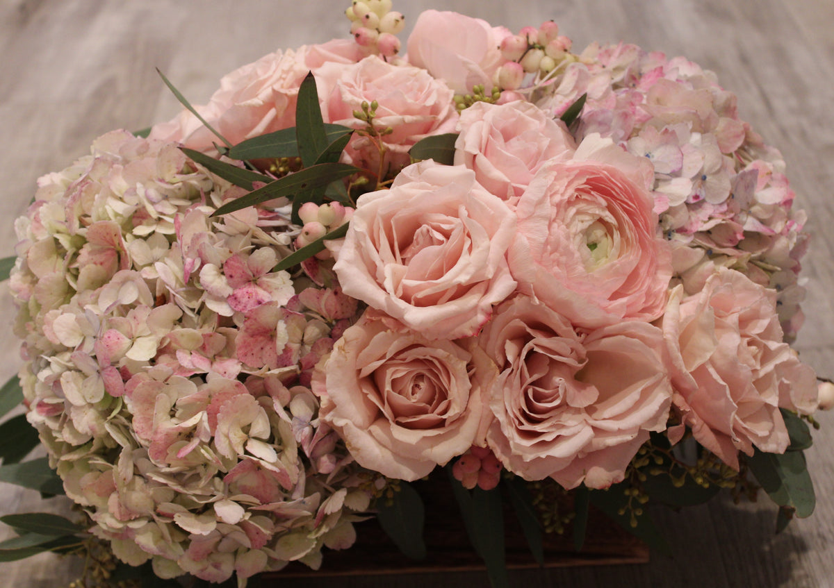 Floral arrangement in pastel pink shades with hydrangeas, pale pink roses, pink snowberries, and seeded eucalyptus