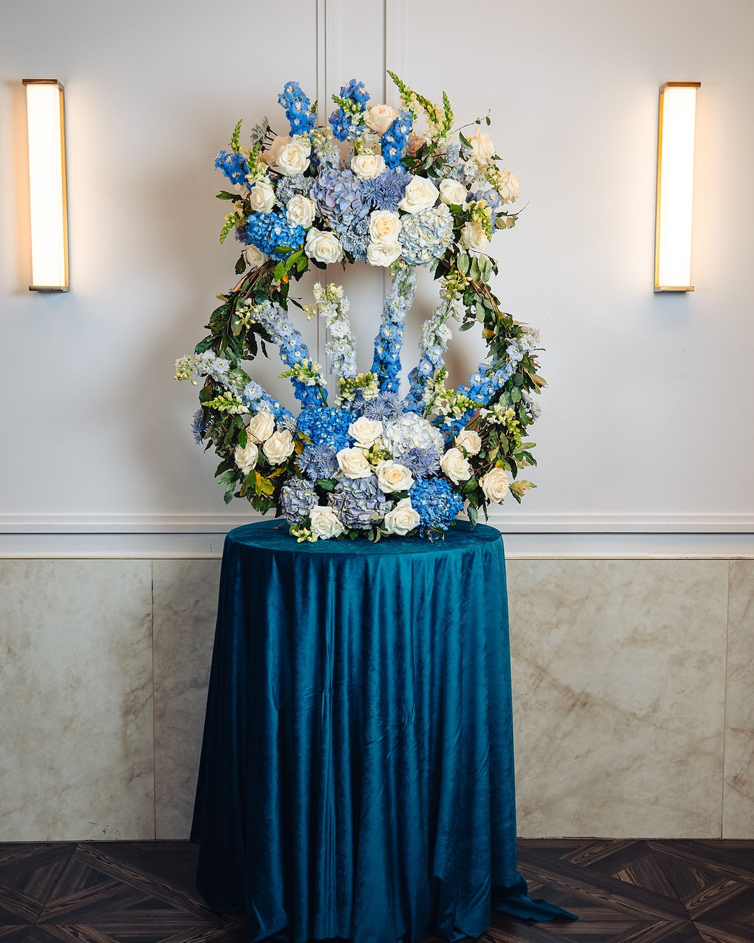 gold ring stand with blue and white floral arrangement containing hydrangeas, delphinium, roses, and snapdragons