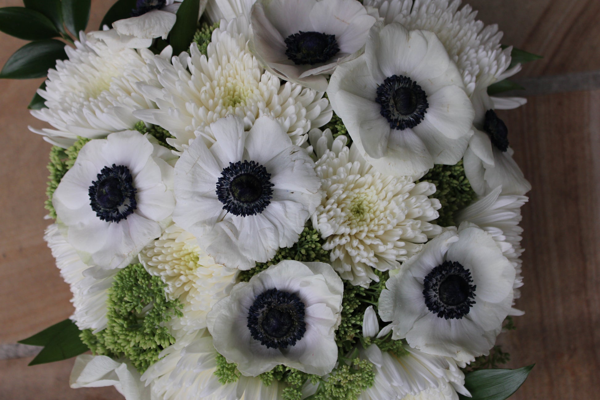 Top view of floral  arrangement of black and white anemones, white spider mums, green sedum, and nagi foliage
