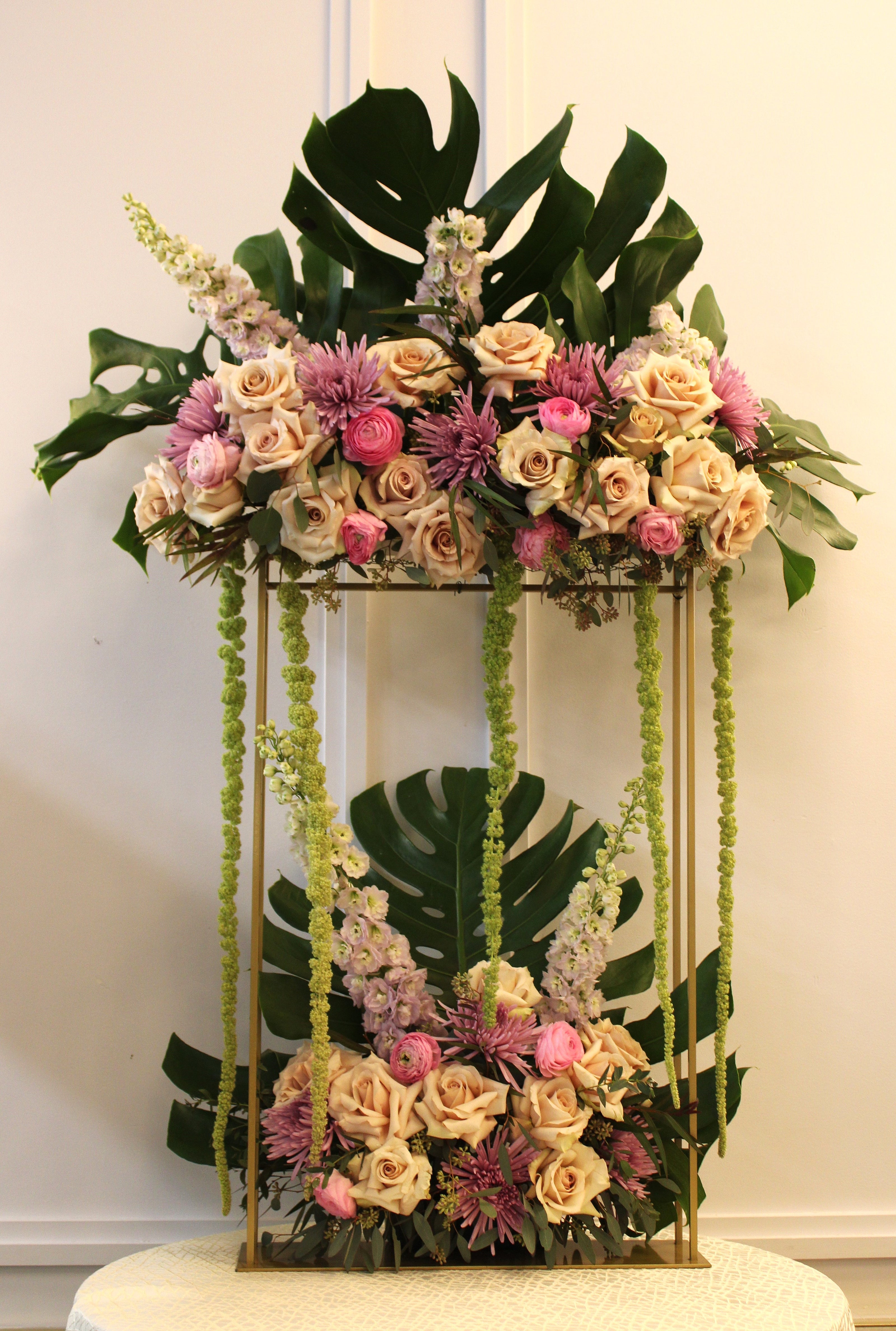 Large floral arrangement for vort with quicksand roses, light pink ranunculus, lavender delphinium, lavender mums, green hanging amaranthus, eucalyptus, and medium monstera leaves