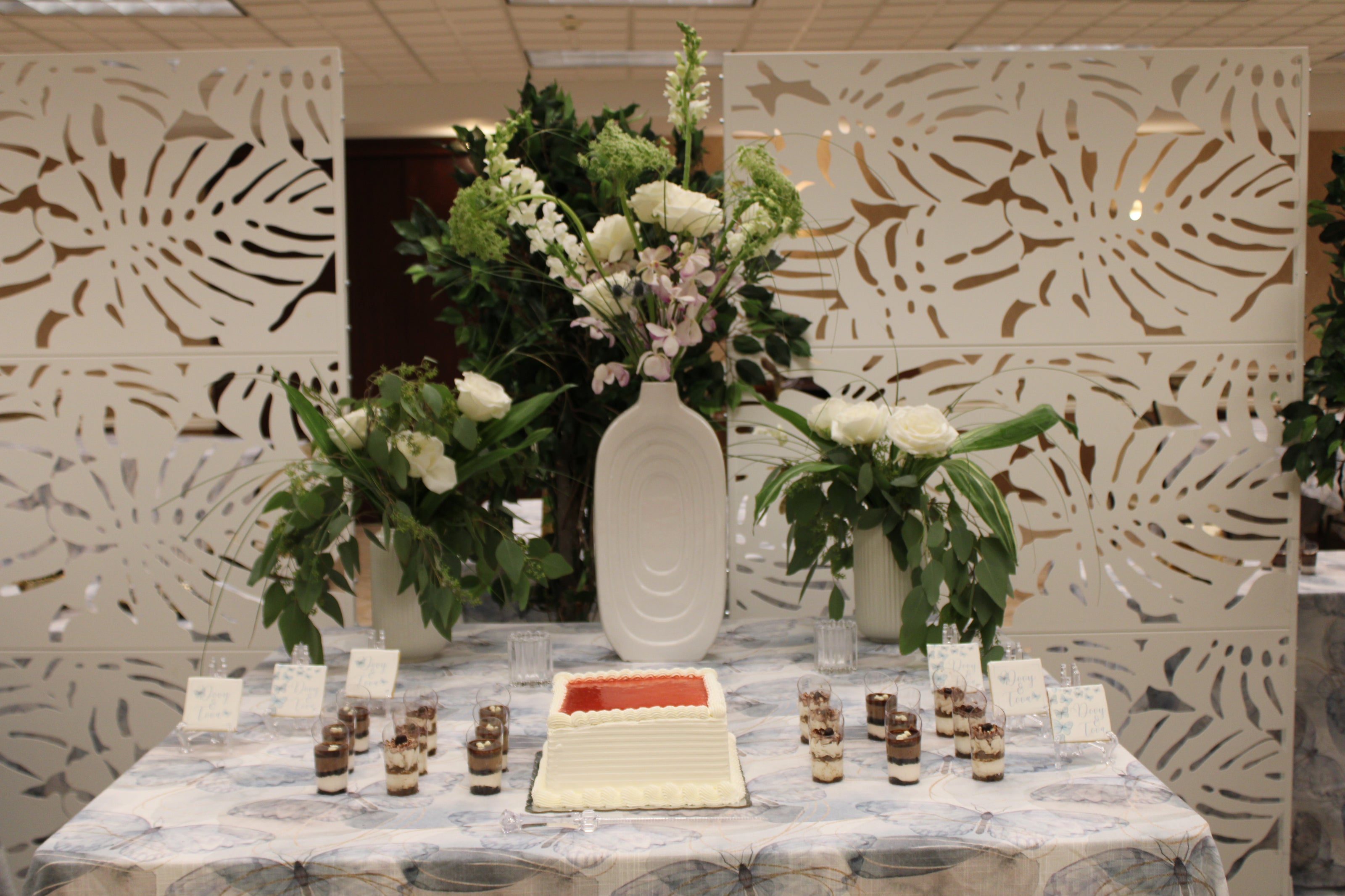 Decorative table setup with floral arrangements of roses, orchids, thistle, Queen Anne's lace, and snapdragons, against patterned backdrop.