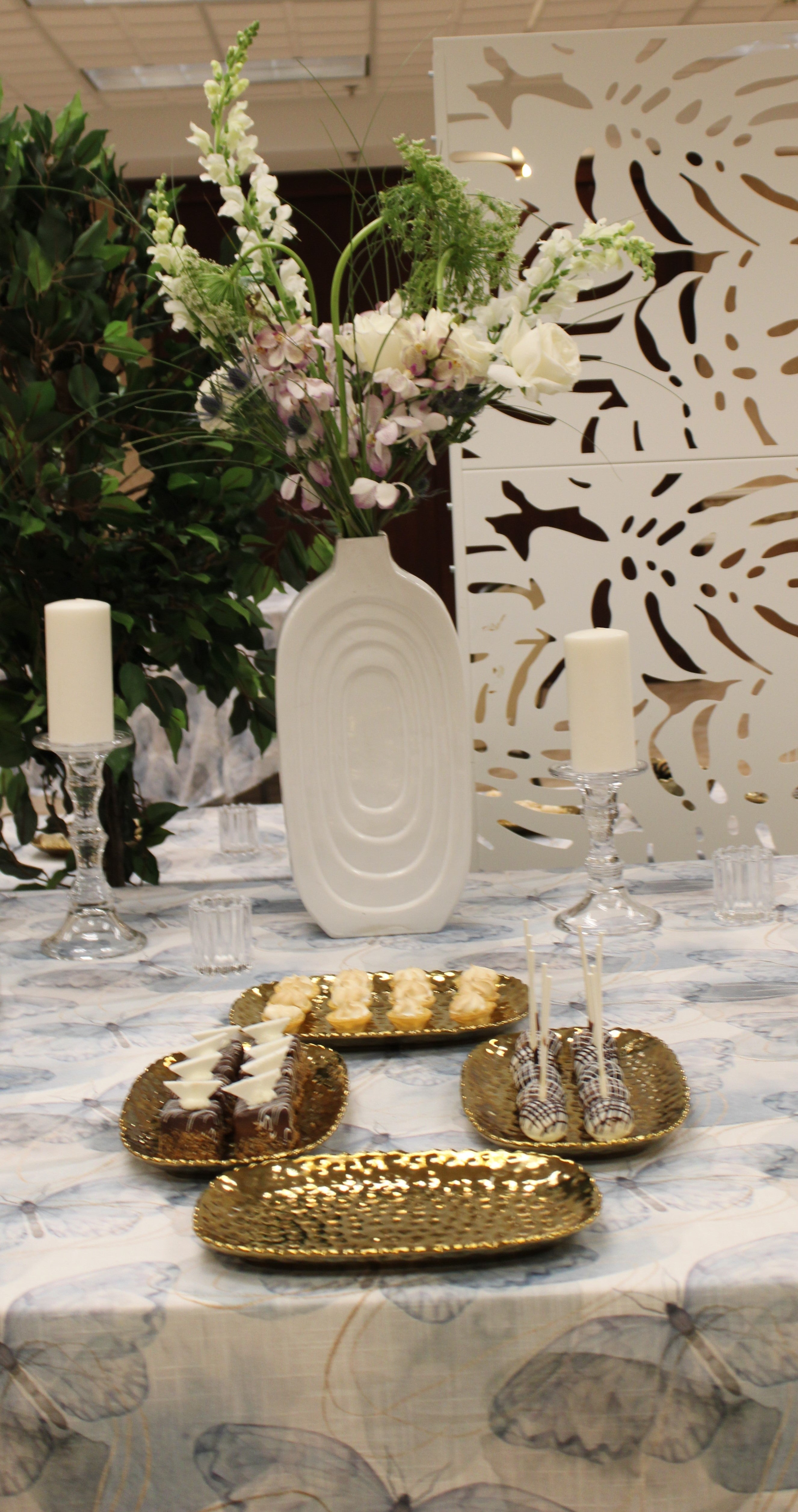 Decorative table setup with bouquet of roses, orchids, thistle, Queen Anne's lace, and snapdragons, against patterned backdrop.