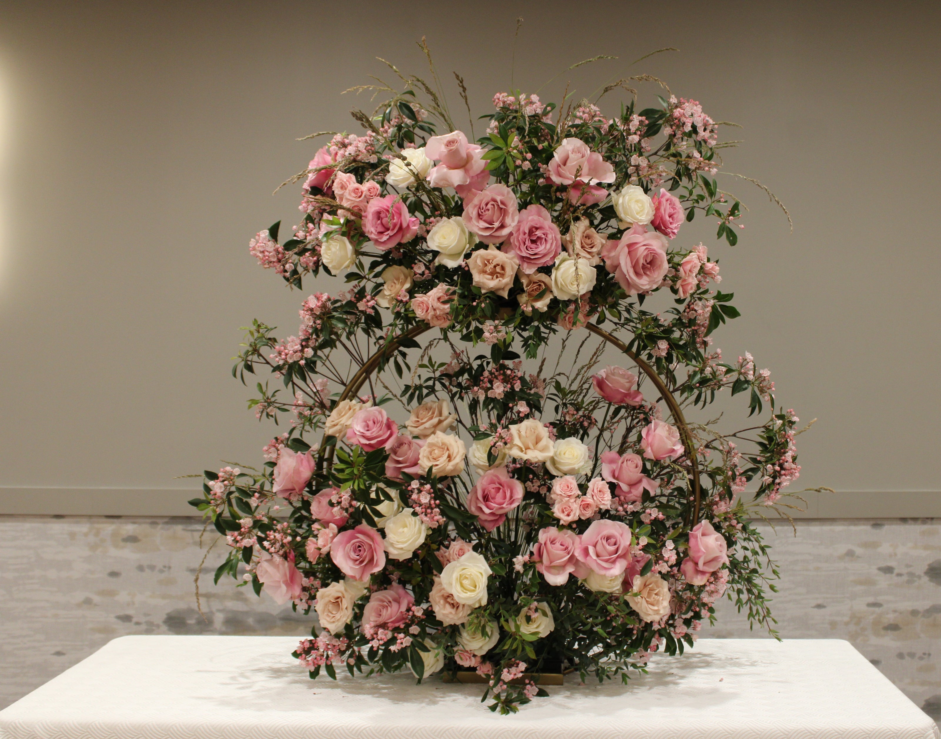 Chosson piece floral arrangement for a vort on a gold ring stand with pink, cream, and sand-colored roses, various foliage, and pink flowering branches