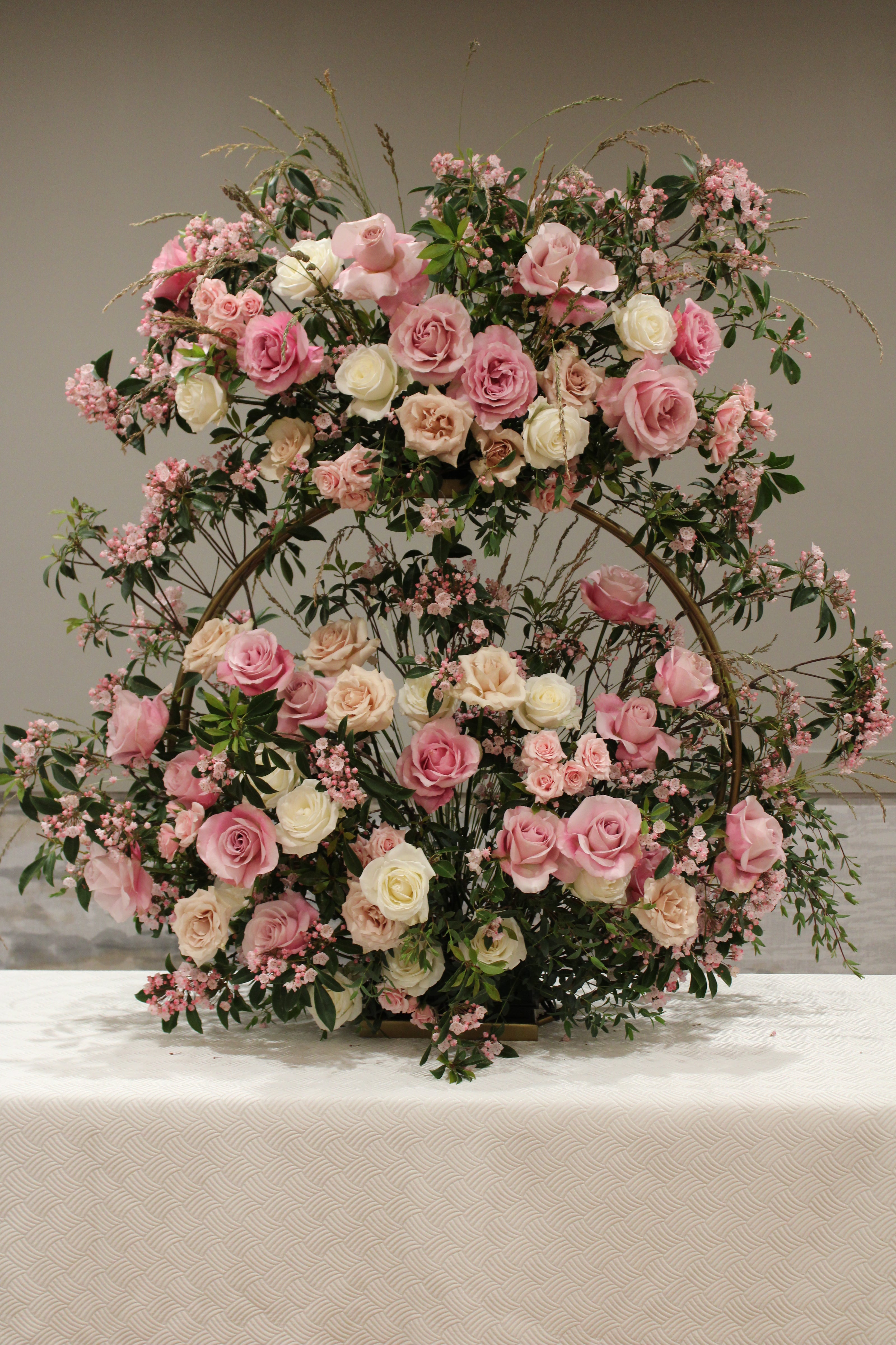 Chosson piece floral arrangement for a vort on a gold ring stand with pink, cream, and sand-colored roses, various foliage, and pink flowering branches