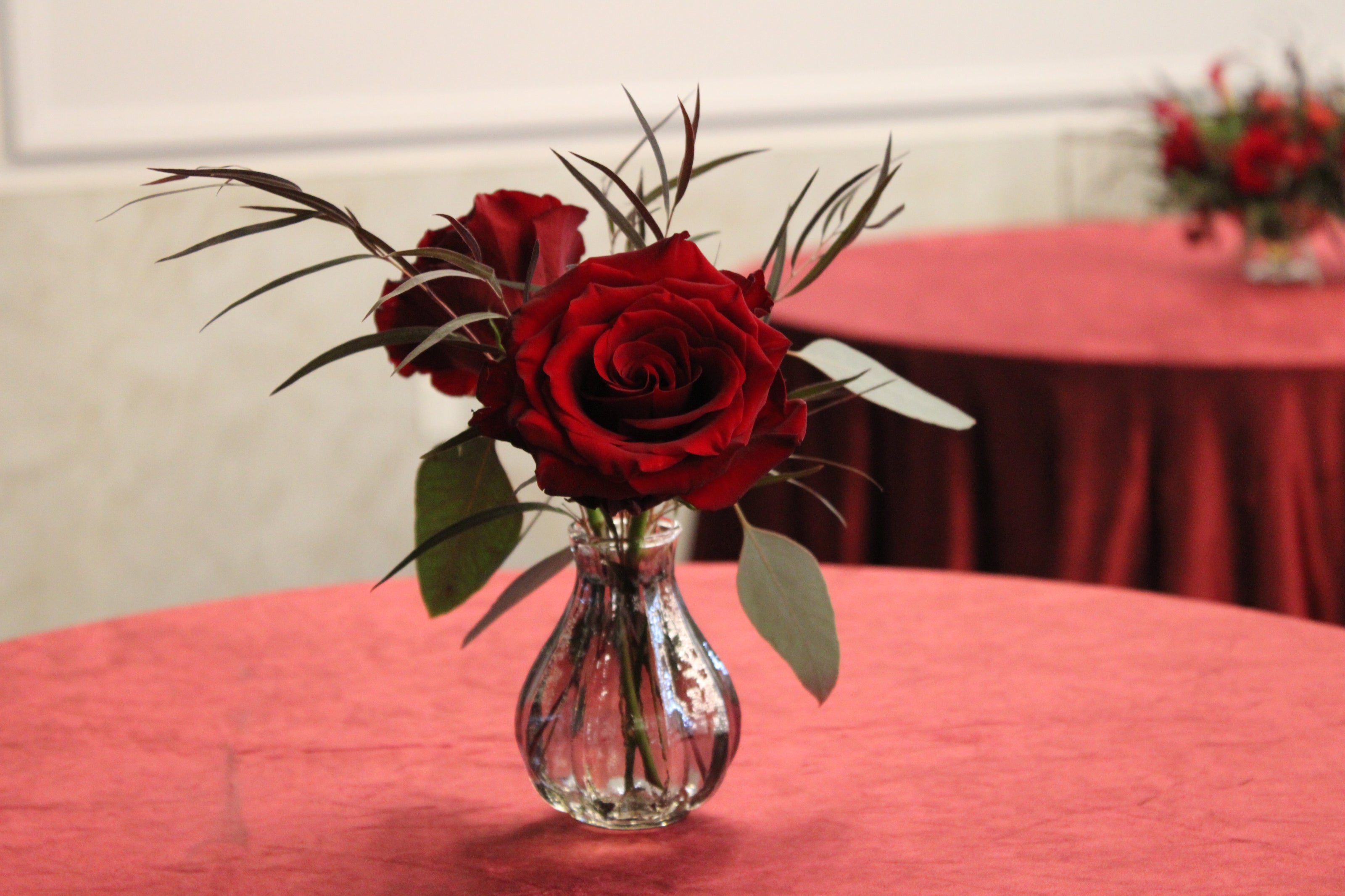 Bud vase with red roses and eucalyptus on a red velvet tablecloth at vort