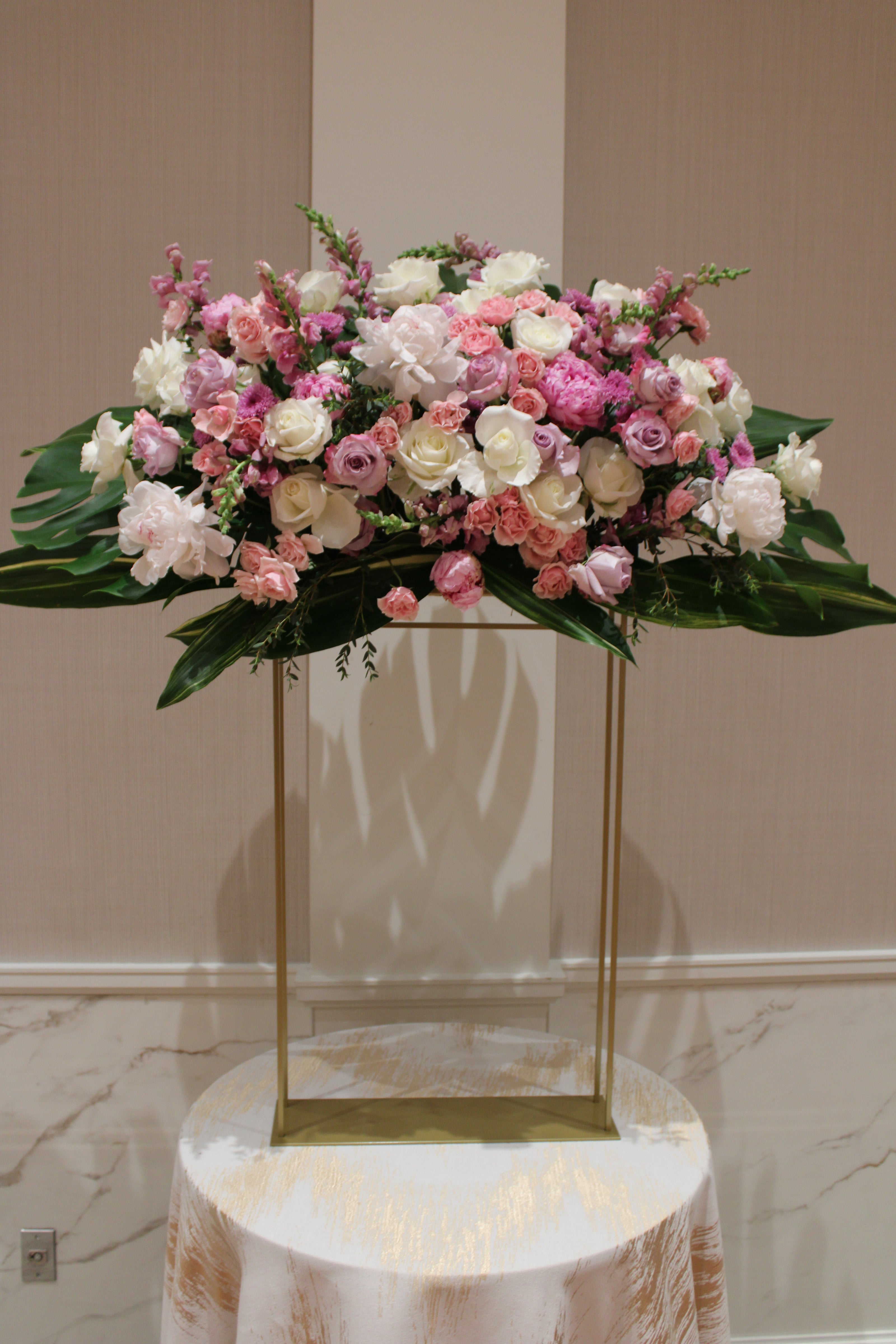 Gold stand with pastel colored pink, purple, and white flowers and big leaves